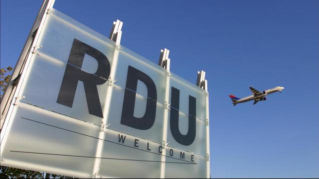 Front sign of RDU airport. An airplane is taking off in the background.