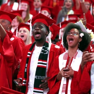 NC State students in red graduation attire in mid-celebration! They are cheering and yelling in a crowd.
